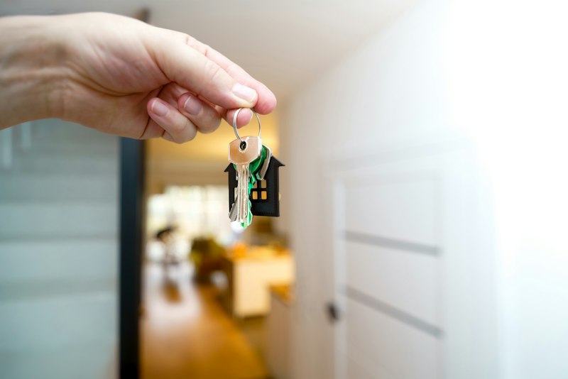 Hand hält den Schlüssel zur neuen Wohnung vor der Eingangstür